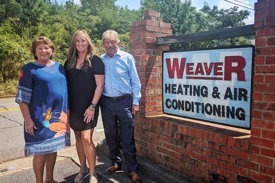 Three owners and operators of Weaver Heating & Air, Inc. standing next to the brick sign in Cartersville, GA